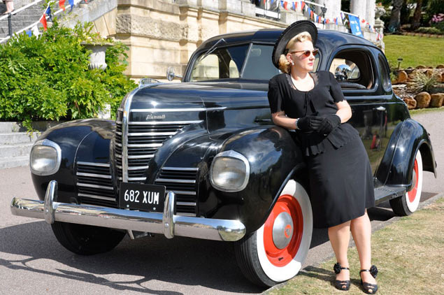 Lady in 1940s clothing leaning on a vintage car